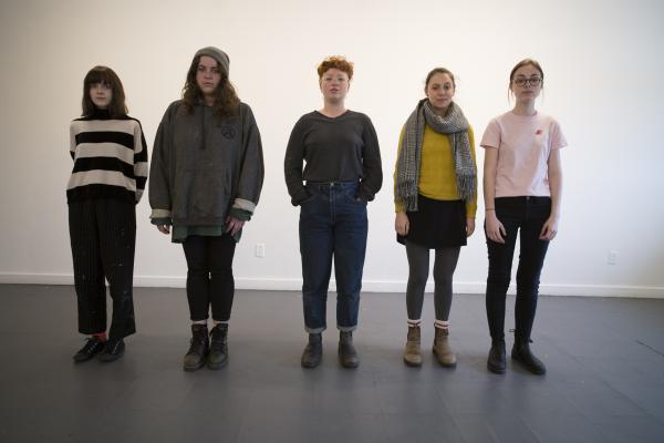A group of people standing against a wall facing the camera