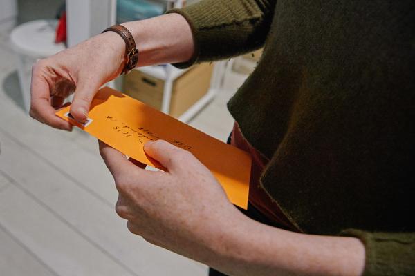 Two hands holding the postcards that are inside of a bright orange envelope, soon on their way to summerland.