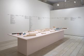 installation view of a long pale pink plinth and sculptural objects