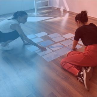 image of two people crouched, working together on the floor. The image is overlayed with a gradient from pale blue to deep orange and the words "RRR remote research residency" in black text.