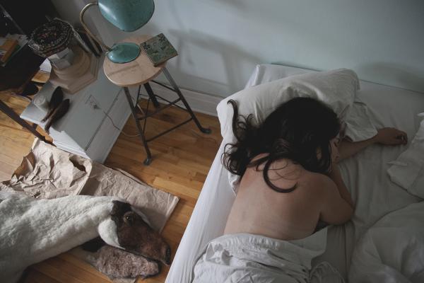 A view from above of a woman laying in bed, with a felt horse on the floor beside her