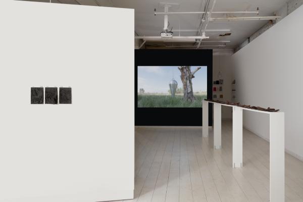 installation view featuring a long narrow shelf topped with steel plates, a video on a dark wall, and small works on paper on a wall