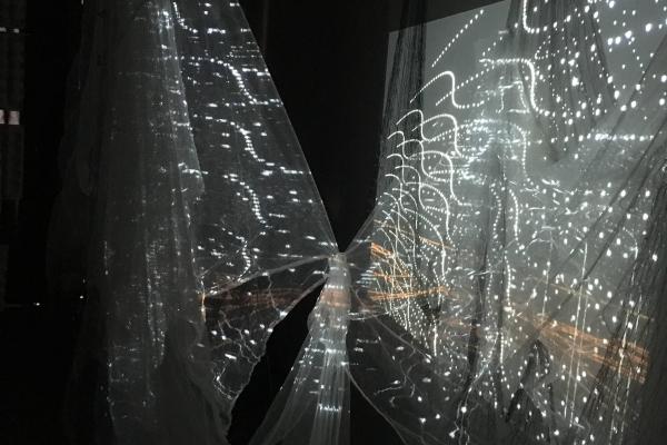 image of a dark space with floating fabric, on which is projected light and drawn lines