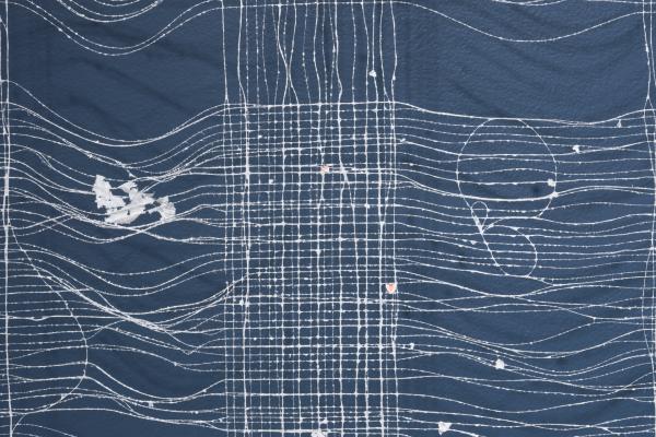 A detail shot of one of the pieces. This is a white weaving which appears to be nylon thread coated in paper pulp. This hangs before a blue wall. 
