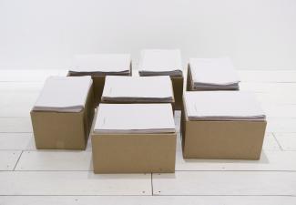 seven cardboard boxes on the floor, each topped with piles of newsprint