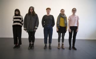 A group of people standing against a wall facing the camera