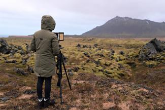 image of the artist and her camera, looking out at a lava field in Iceland.