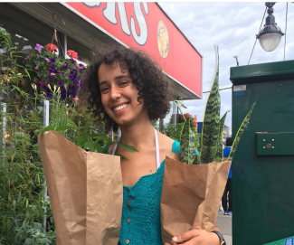 A smiling person holding paper bags filled with plants