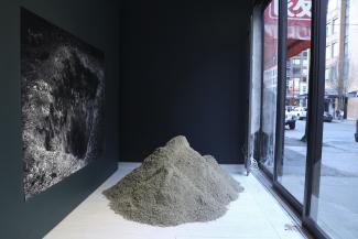 Installation view of pile of sand with photograph of hole in dirt.