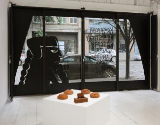 View through a window from inside the gallery, featuring plaster sculpture and vinyl window installation