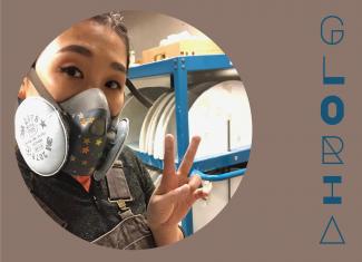 Circular image of Gloria "smizing" through a particulate mask, standing in a ceramic's studio signing two fingers in a V, placed in a taupe background with her stylized name in dark blue to the right.