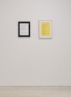 Image of a white wall on which hung two document-sized prints, one white and one yellow.