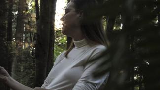 Image of a person standing in a forest wearing a white shirt