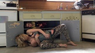 A mother holding her children while climbing out of a lower kitchen cupboard as if dancing