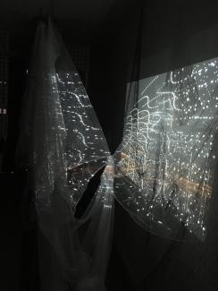 image of a dark space with floating fabric, on which is projected light and drawn lines