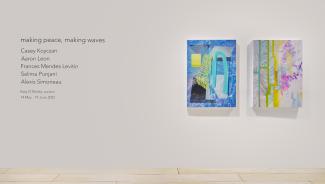 Black vinyl lettering on the left of a wall and two bright paintings on the right. The lettering reads the exhibition title, artists' and curator's names, and exhibition dates. The paintings are abstract in blues, yellows, and pinks.
