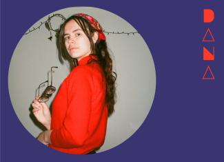 Circular image of head shot of Dana, wearing a bright red sweater and bandana, standing turned one quarter away from the camera, looking back. The portrait is placed in a dark purple background with their stylized name in bright red to the right.