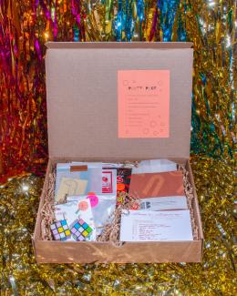 Image of a n open cardboard box filled with treats, photographed against a colourful streamer background.