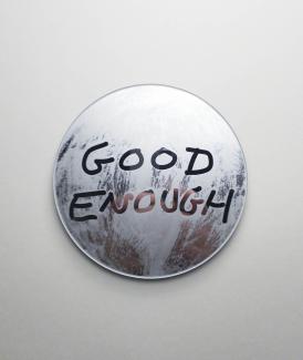 A small circular mirror against a white backdrop. The mirror has been etched with the words GOOD ENOUGH as negative space