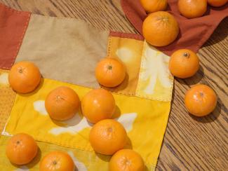 On a wooden table lays a bright yellow Bojagi (traditional Korean wrapping cloth), and a number of bright orange tangerines.