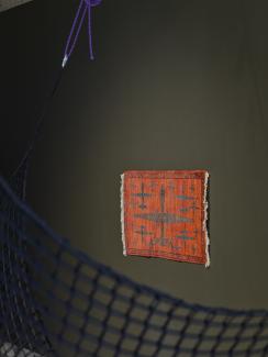 Another angle shows the Weaver's rust-red rug with predator drones in the background of the image, with the edge of a cargo net (part of Serena Lee's sound installation) cutting through the foreground. 