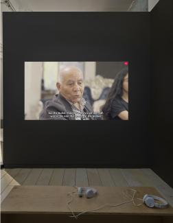 An older man looks down in a video work by Forensic Architecture. Captions pick up mid-sentence, reading: "... but the burial, God have mercy on them all, was in the kiln that was near the bodies."
