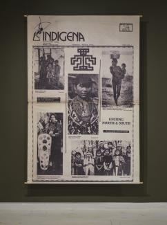 A large canvas prints stretches from floor to ceiling in the gallery. The print shows the cover spread of Indígena: News From Indian America, and contains five photos of Indigenous women along with the text "Uniting North & South" . 